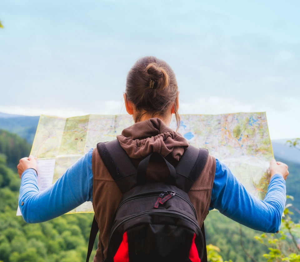 Hiking woman traveler with backpack checks map to find directions in wilderness area, real explorer. Travel Concept