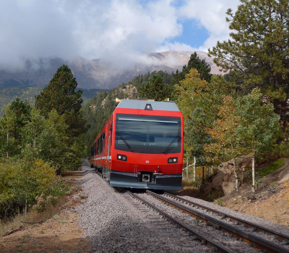 Red train on railway tracks with green and yellow trees in background