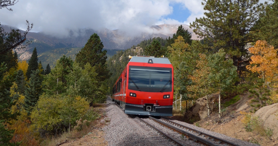 Red train on railway tracks with green and yellow trees in background