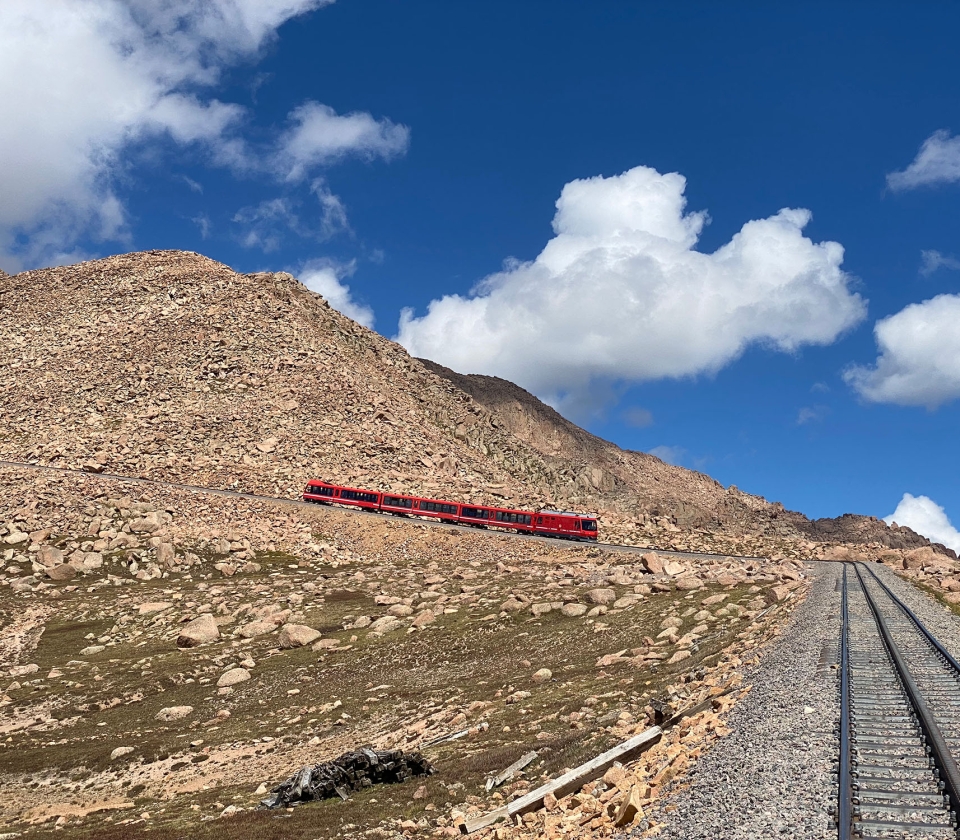 Red train coming down mountain on sunny day with blue skies