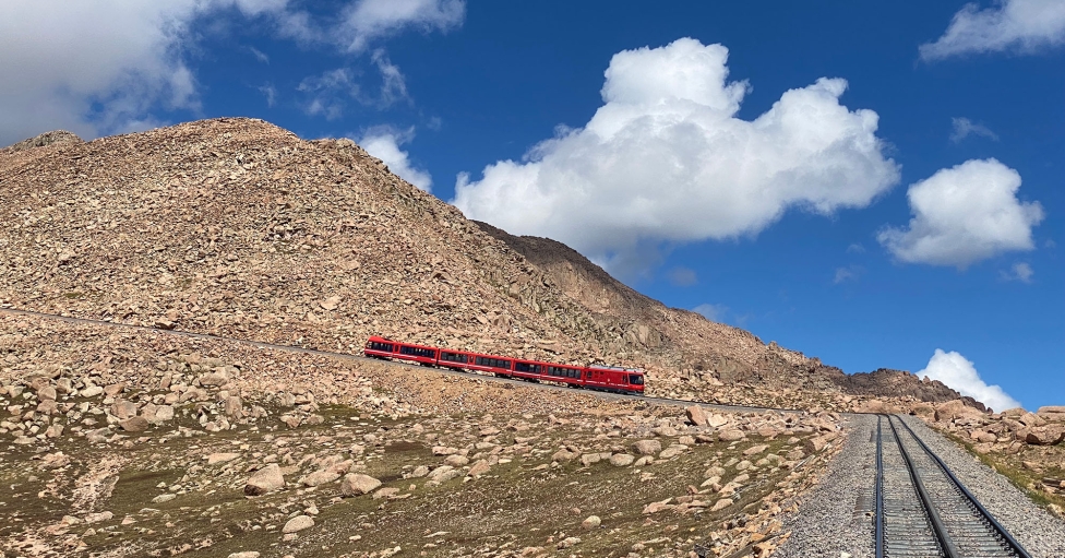 Red train coming down mountain on sunny day with blue skies