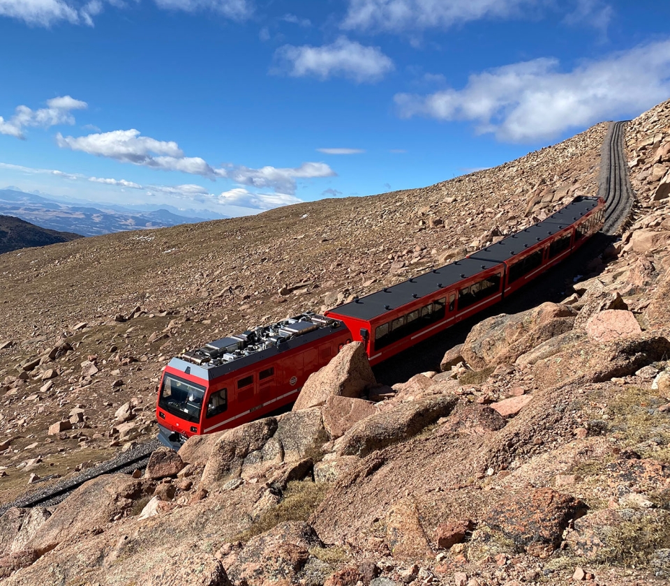 red train coming down mountain on sunny day