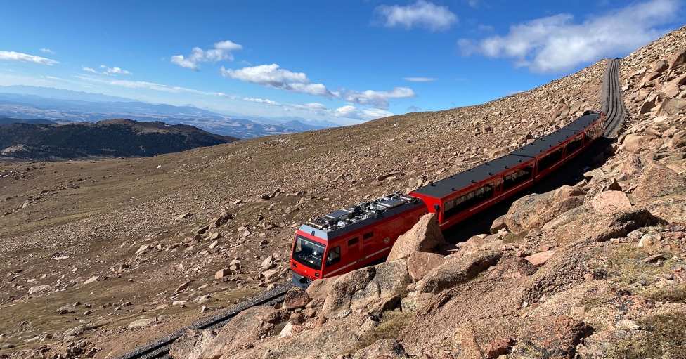 red train coming down mountain on sunny day